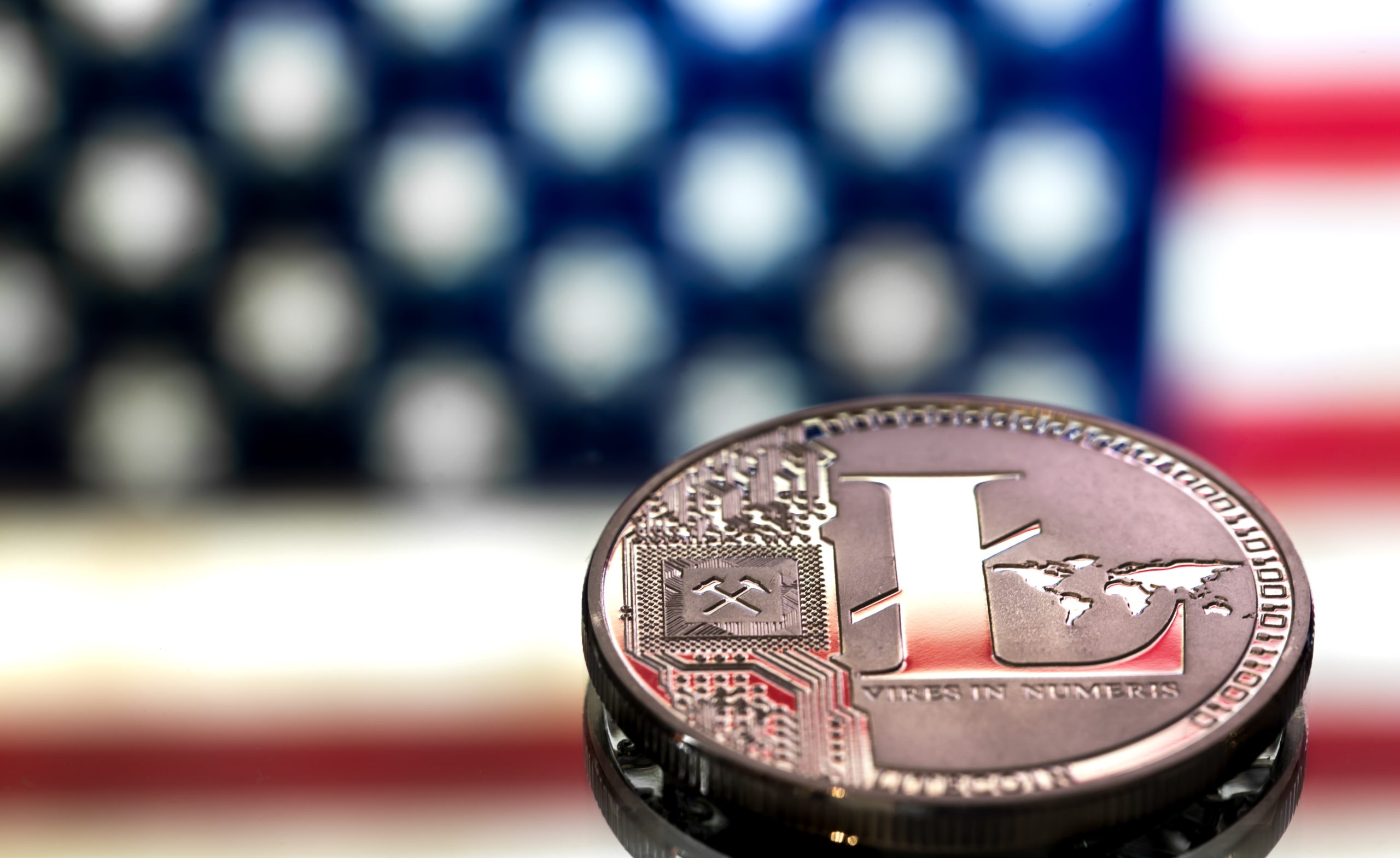 A close-up image of a Litecoin coin with a digital design, set against a blurred American flag background, symbolizing the concept of virtual money and cryptocurrency.