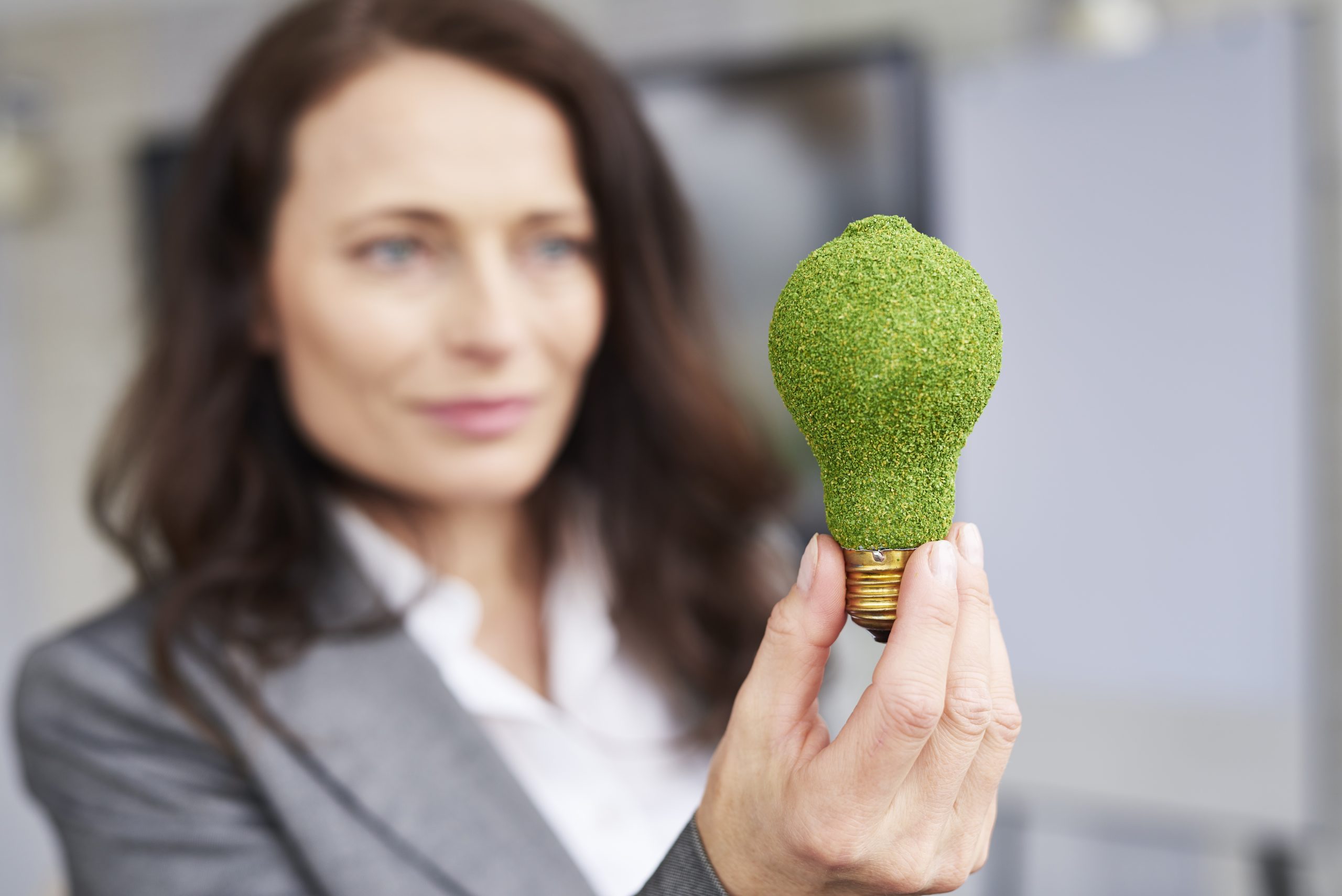 A woman holding a light bulb designed to look like it is made of grass, symbolizing the concept of renewable energy and sustainability.
