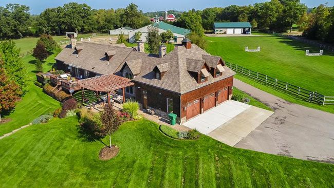 A spacious countryside property with a large house, green lawns, and farm buildings surrounded by fences and trees, representing the charm and investment potential of rural real estate.