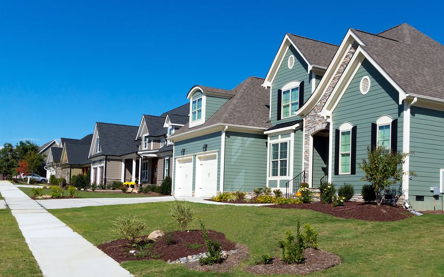 Row of modern suburban houses with well-kept lawns under a clear blue sky, representing real estate investment and the growth of residential property value.