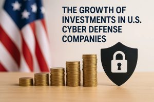 A conceptual financial illustration featuring a series of stacked gold coins arranged in ascending height on a wooden surface, symbolizing the growing value of investments. To the right of the stacks, a black shield icon with a white padlock in the center represents cybersecurity and data protection. In the blurred background, the U.S. flag adds national context. At the top, bold text reads: ‘The Growth of Investments in U.S. Cyber Defense Companies.’ The composition visually highlights the increasing financial commitment to cybersecurity firms in the United States.